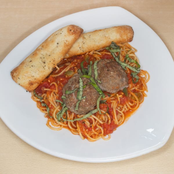 Spaghetti with meatballs, tomato sauce, basil, and two breadsticks on a white plate.