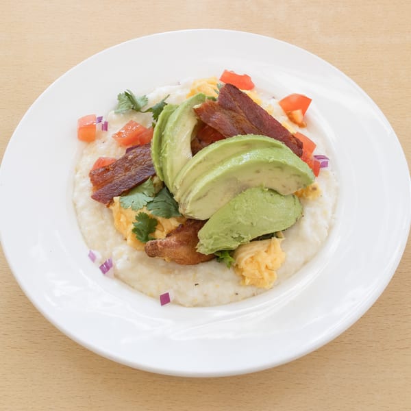 Grits topped with scrambled eggs, bacon, avocado slices, diced tomatoes, and red onion.