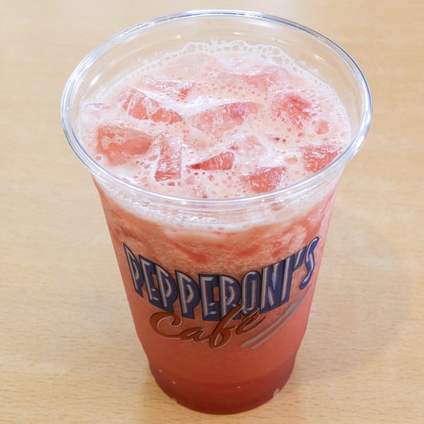 A Pepperoni's Cafe plastic cup filled with a pink, icy, foamy drink on a wooden table.