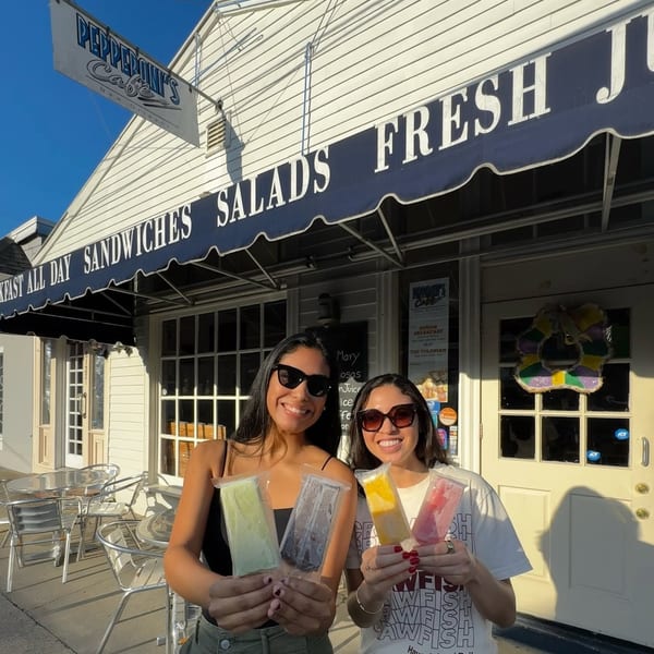 Two smiling women holding colorful frozen treats in front of Pepperoni's Cafe in New Orleans.