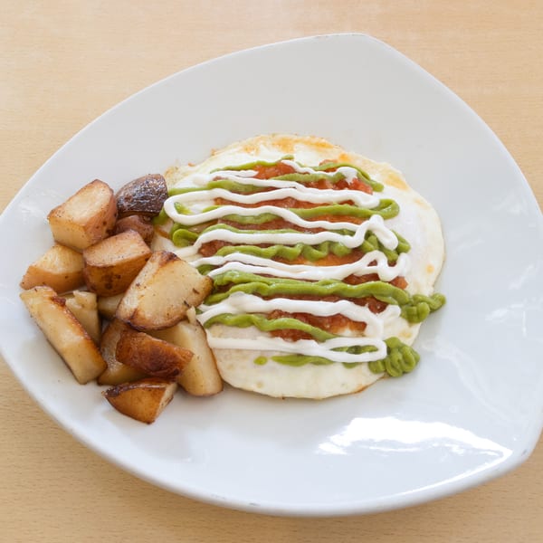 Huevos rancheros with salsa, avocado crema, and sour cream, served with roasted potatoes.