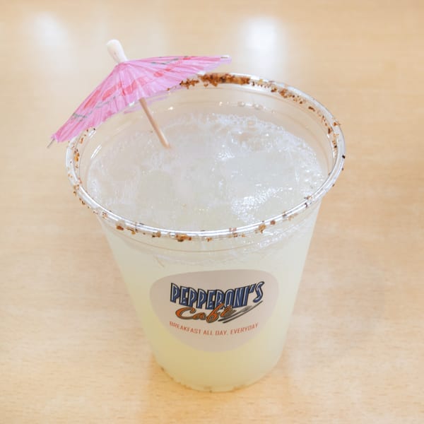 A Pepperoni's Cafe frozen drink with a spiced rim and a pink umbrella on a wooden table.
