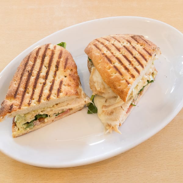 Two halves of a grilled panini sandwich with melted cheese, turkey, and spinach on a white plate.