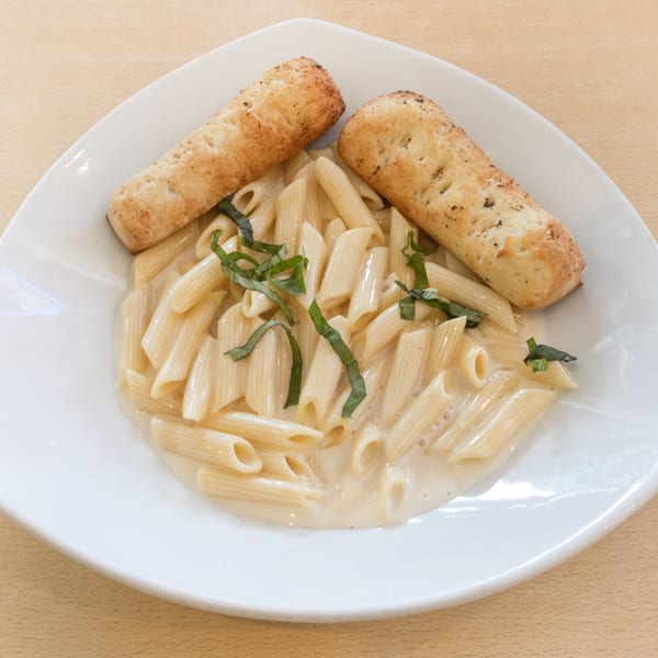 Penne pasta in a creamy sauce with basil and two breadsticks on a white plate.