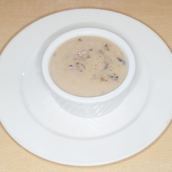 Creamy mushroom soup in a white ramekin, served on a white plate on a wooden table.